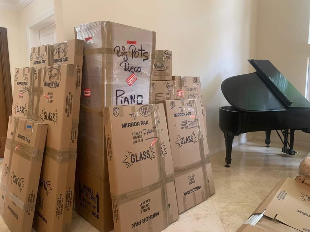 Expertly packaged boxes with a piano behind. moving company in Fernandina Beach
