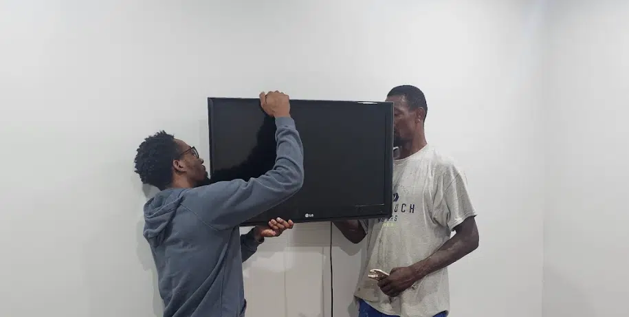 Services 28 Two Pro Touch Movers employees expertly mounting a TV onto a wall.
